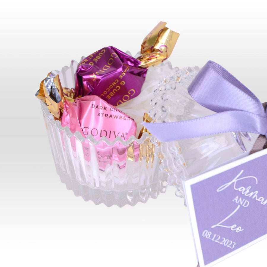 A VWOWGIFTS Sweet Blessing wedding favor with Crystal Glassware Box, a purple ribbon, and chocolates.