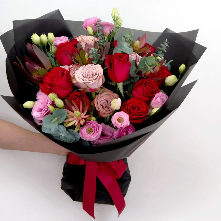 A hand holding a bouquet of VWOWGIFTS CLASSIC RED roses.